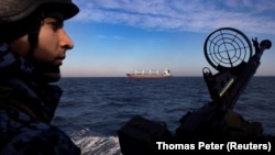 Член на украинската брегова охрана на патрулна лодка, докато товарен кораб минава покрай нея в Черно море през февруари 2024 г.