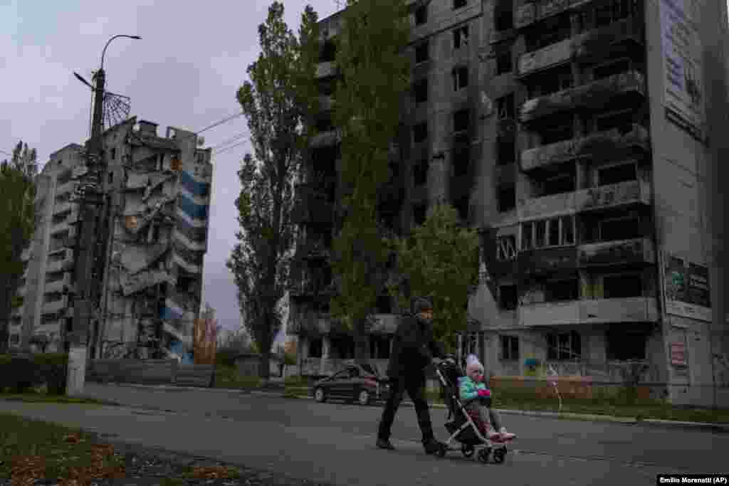 Чоловік штовхає візок з дитиною, йдучи повз зруйновані житлові будинки у Бородянці, Київщина. У деяких із будинків є електрика, інші люди залишилися повністю без електрики та води й зараз готуються до суворої зими 