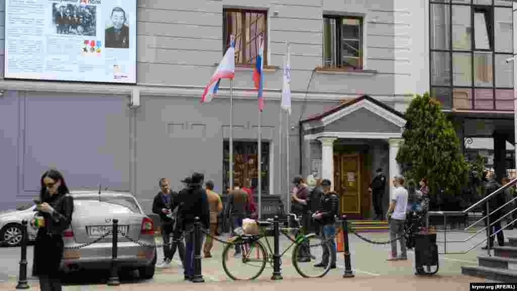 Черга перед відділенням банку «Росія» на проспекті Кірова у Сімферополі. Щоб люди не нудьгували, їм транслюють на великому екрані, встановленому на фасаді будівлі, документальний фільм «Безсмертний полк»